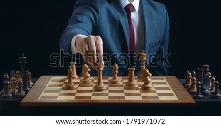 Hand of man un suit moving chess figure on board on black background. Close up of male player making tactic move with white piece during chess tournament Royalty-Free Stock Photo #1791971072
