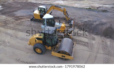 Construction machinery: aerial view of an excavator, roller compactor, bulldozer on a construction site Royalty-Free Stock Photo #1791978062