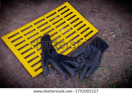 Yellow ventilation grill and black gloves on the ground. Abstract background.