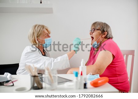 Doctor taking a sample from a mature woman's throat using a cotton swab