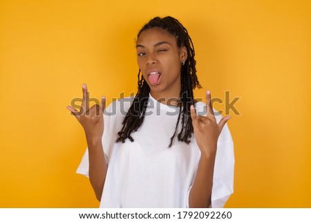 Young  dark skinned woman with braids hair wearing casual clothes posing in studio. showing rock and roll hand gesture 