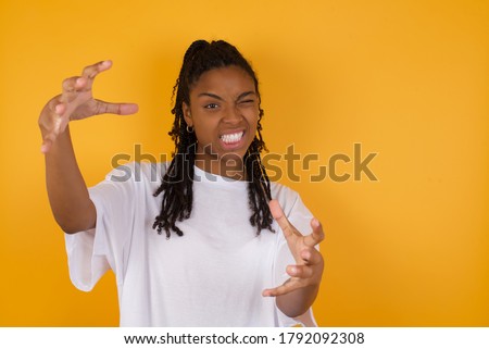 Young  dark skinned woman with braids hair wearing casual clothes Shouting frustrated with rage, hands trying to strangle, yelling mad.
