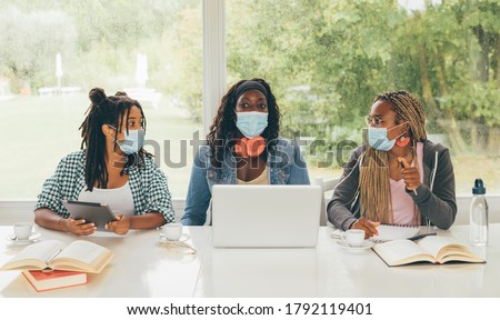 Three African American girls (students) sitting at the table studying up for test or making homework together, they are using laptop and digital tablet, wearing surgical masks. Back to school concept. Royalty-Free Stock Photo #1792119401
