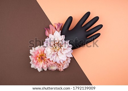 Black rubber glove decorated with fresh flowers. Fall aesthetic in pastel palette. Contrast brown and pastel peach background with abstract details. Pandemic medical rubber glove protects nature.