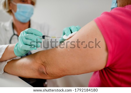 Female doctor makes vaccination to woman.They are wearing a protective face masks. Royalty-Free Stock Photo #1792184180