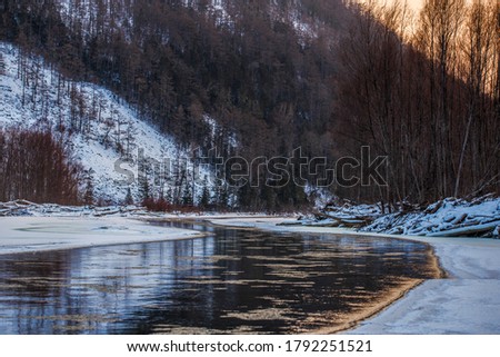 Northern landscape of Primorsky Territory, Samarga River. Frozen river in the taiga against the background of hills with coniferous trees at sunset