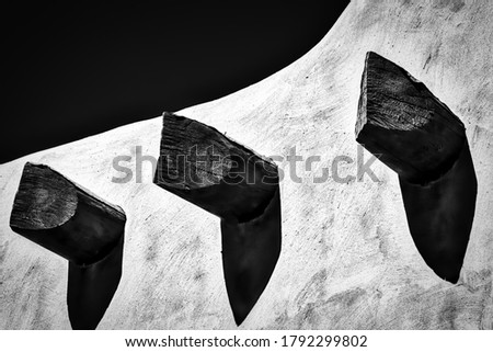 A black and white photo of three vigas and shadows on an adobe wall in Santa Fe, New Mexico.