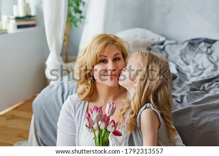 Happy mother's Day. A child-daughter congratulates her mother and gives her flowers and tulips. The child kisses his mother on the cheek. Family holiday and unity