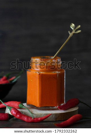 Singapore Chili Sauce on Dark Background with Copy Space. Gold Spoon Scooping Chili. Super Spicy Chili Sauce in a Jar.