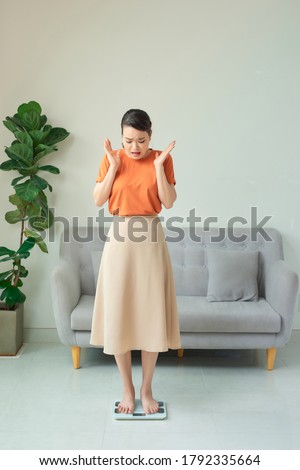 picture of unhappy woman on scales in living room. Weight loss diet