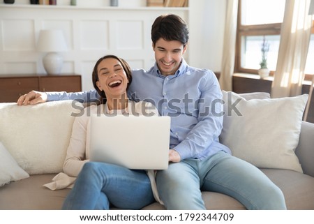 Emotional loving young couple relaxing on comfortable couch, watching funny videos on computer or laughing at comedian movie film, enjoying spending stress free leisure weekend time together indoors. Royalty-Free Stock Photo #1792344709