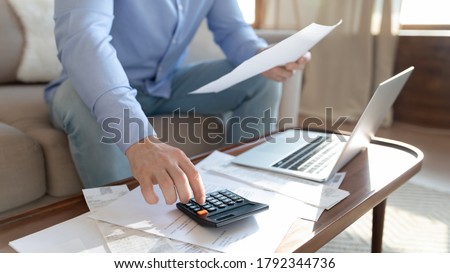 Close up young man holding paper bills, calculating monthly household expenditures alone at home, focused guy managing incomes and outcomes, paying taxes, considering financial paperwork indoors. Royalty-Free Stock Photo #1792344736