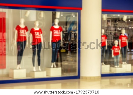 Blurry conceptual background. Many mannequins wear a red shirt with the word "sale." There is a stand in front of the store. Pictures of concepts sale, shopping