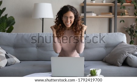 Overjoyed young female in glasses look at laptop screen feel euphoric with online lottery win or success, excited woman in eyewear triumph read pleasant good news in email on computer, luck concept Royalty-Free Stock Photo #1792419700
