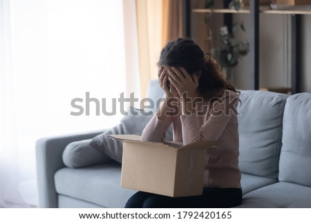 Unhappy millennial girl client unbox cardboard package with internet order disappointed with bad poor quality or wrong goods, upset young woman customer feel frustrated shopping buying online Royalty-Free Stock Photo #1792420165
