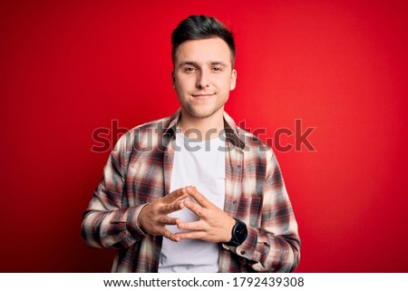 Young handsome caucasian man wearing casual modern shirt over red isolated background Hands together and fingers crossed smiling relaxed and cheerful. Success and optimistic