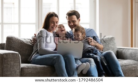 Happy bonding family sitting on cozy sofa, enjoying watching funny comedian movie on laptop at home. Overjoyed young family couple having fun, laughing at cartoons, spending weekend time together.
