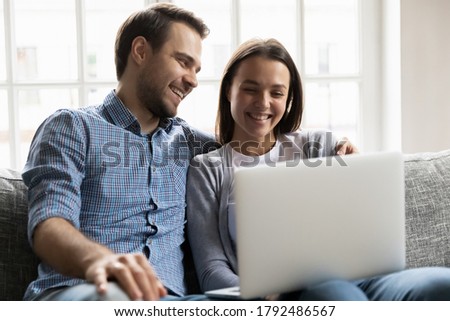 Happy loving young man cuddling smiling pretty wife, watching comedian movie or funny TV series on laptop. Emotional joyful bonding couple looking at computer screen, web surfing or shopping online. Royalty-Free Stock Photo #1792486567