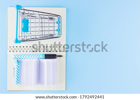 Back to school concept. Shopping cart and stationery on blue background. Pen, notepad and shopping trolley. Time to study. Top view