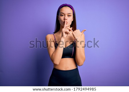 Young beautiful sporty girl doing sport wearing sportswear over isolated purple background asking to be quiet with finger on lips pointing with hand to the side. Silence and secret concept.