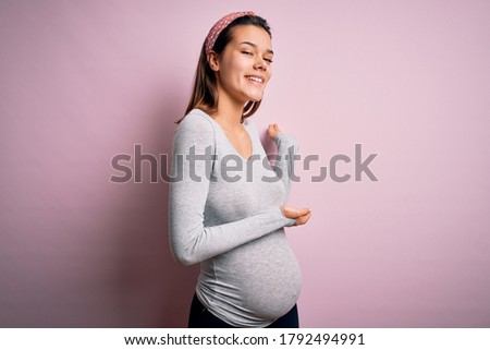 Young beautiful teenager girl pregnant expecting baby over isolated pink background Inviting to enter smiling natural with open hand