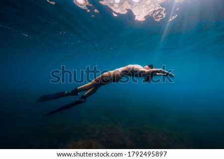 Woman freediver with fins relaxing in blue sea. Woman underwater and reflection