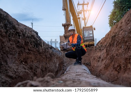 Engineer wear safety uniform examining excavation water supply or sewer pipeline at construction site. Royalty-Free Stock Photo #1792505899
