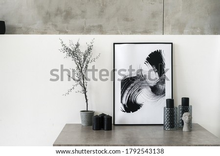 Table with home decor in living room. Modern interior house with abstract painting in frame, houseplant, candles, vase and decorative statuette against white concrete wall
