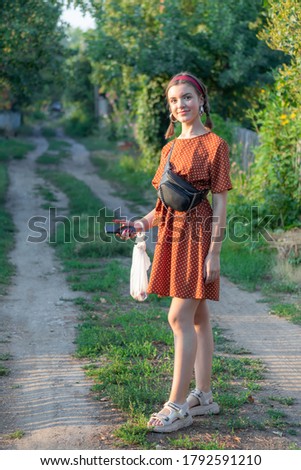 A young girl with pigtails in a bright dress in the village in nature.