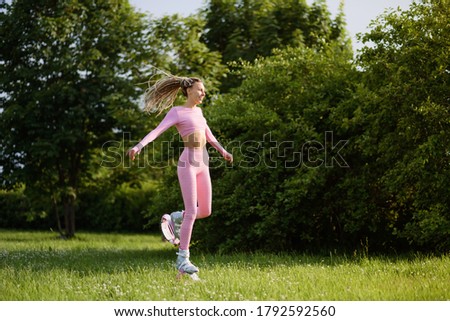 A young slender beautiful woman with dreadlocks in sportswear, pink T-shirt and short shorts trains in the park outdoors. Kangoo jumps training.