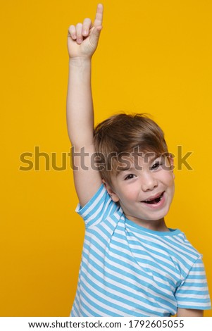 Little cute boy in a blue and white striped T-shirt points his finger at the outstretched hand, isolated on a yellow background.