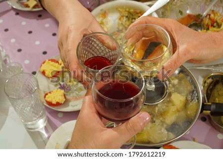 Glasses with red and white wine in three hands clink against the background of the festive table.                               