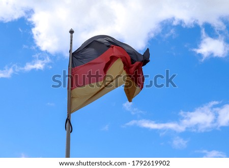 Germany flag at a flagpole moving in the wind against the sky