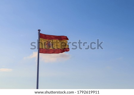 Spain flag at a flagpole moving in the wind against the sky
