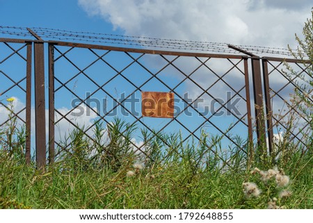 Rusty fence section with installed old rusty barbed wire and old warning sign