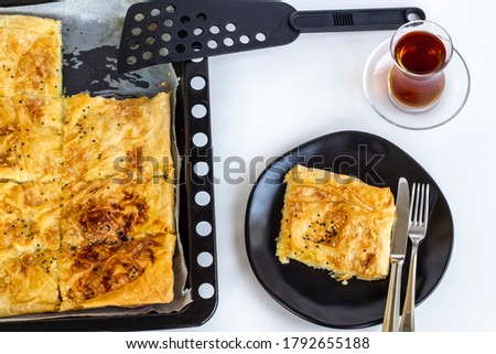 Traditional Turkish homemade tray pastry sliced in metal tray of oven on white with plate,cutlery set and tea.