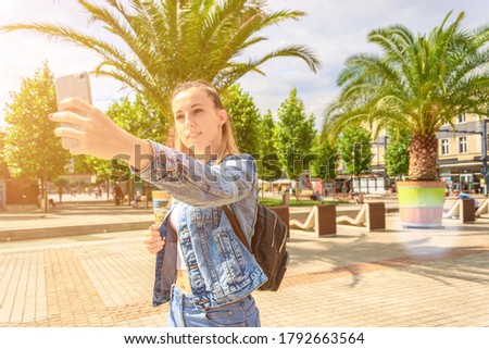 Making picture. Pretty female taking fun self portrait photo. Happy young girl with phone smile, typing texting and taking selfie in summer sunshine urban city. Vanity, social network concept.