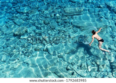 A woman swims in blue sea water in the bay. Nature and relaxation, top view.