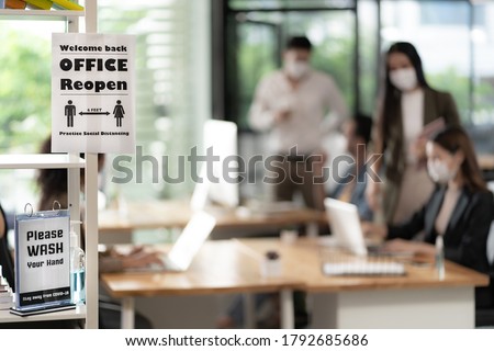 Signage of Office Reopen with social distancing practice with blurred background of Asian team business people working and wear face mask in new normal office to prevent covid-19 virus spreading. Royalty-Free Stock Photo #1792685686