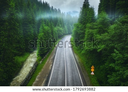Aerial view of road in beautiful green forest in low clouds in rainy summer day. Colorful landscape with roadway in fog, pine trees, river in Carpatian mountains. Top view of road. Travel in Ukraine Royalty-Free Stock Photo #1792693882