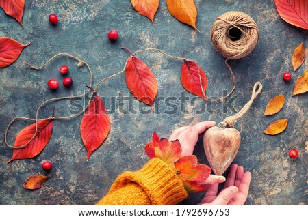Hands in orange sweater hold wooden heart. Natural Fall decorations, vibrant red, yellow oak leaves. Flat lay on dark background. Charity concept.