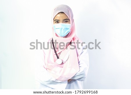 Muslim female doctor with hijab wearing mask to protect virus and standing with confidence on white background. Medical and New Normal Concept.