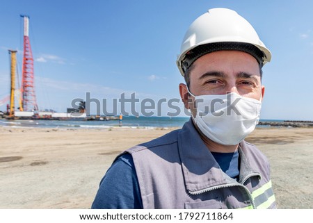 The worker is looking at the camera with facemask in the construction site.