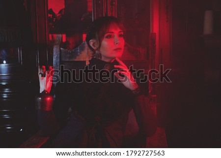 Redhead girl in dark dress posing against different backgrounds in red light