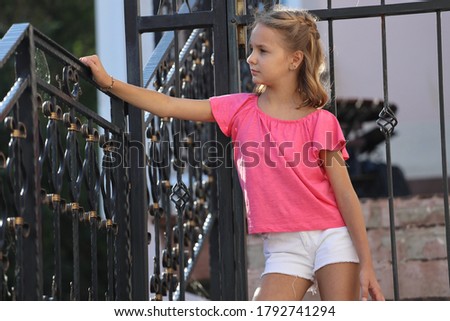 a young girl in a pink t-shirt stands on the steps of a house with colored bags