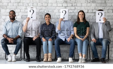 Smiling diverse candidates applicants sitting in row with unknown people holding paper sheets with question marks, successful hired man and women getting job, employment and recruitment concept Royalty-Free Stock Photo #1792768936