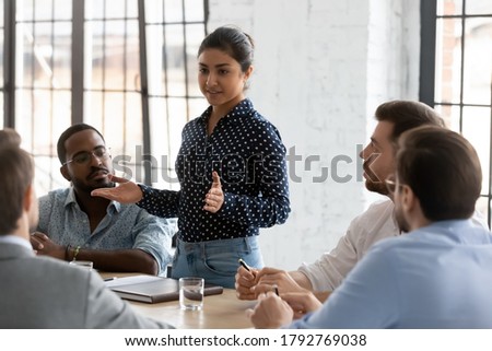 Confident Indian businesswoman mentor coach training staff, speaking at corporate meeting, holding briefing with diverse colleagues, employees, business partners negotiations in boardroom Royalty-Free Stock Photo #1792769038