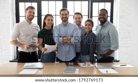 Corporate photo smiling diverse employees with confident executive wearing glasses standing in modern office room, looking at camera, successful startup founder with team, staff members Royalty-Free Stock Photo #1792769173