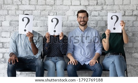 Confident smiling businessman wearing glasses sitting in row with diverse unknown people holding paper sheets with question marks, successful candidate getting job, employment and recruitment concept Royalty-Free Stock Photo #1792769188