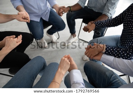 Close up diverse people sitting on chairs in circle at group training counselling session, holding hands, psychological help and treatment concept, drug or alcohol addiction rehabilitation Royalty-Free Stock Photo #1792769566